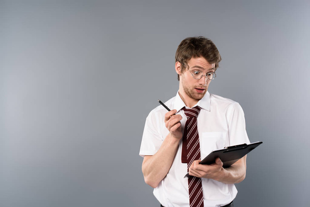shocked man with pen holding clipboard on grey background - Foto, immagini