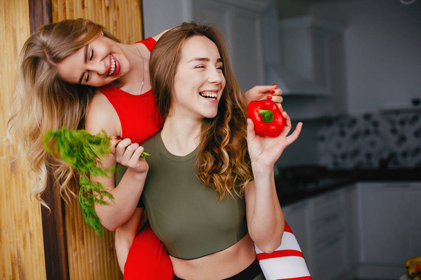 Two sports girl in a kitchen with vegetables - 写真・画像