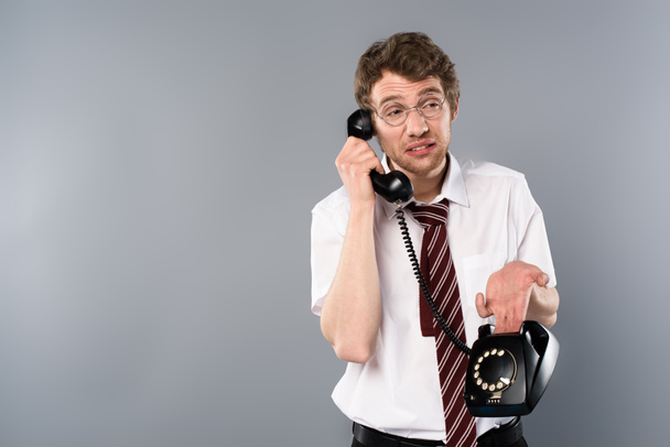 verward zakenman in glazen praten over vintage telefoon op grijs - Foto, afbeelding