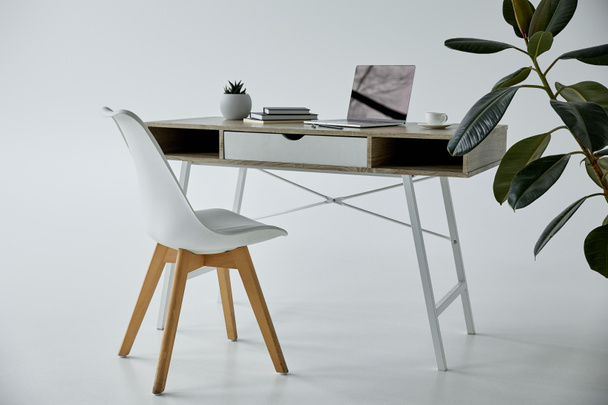 work table with laptop, books, flowerpot and white chair on grey - Фото, изображение
