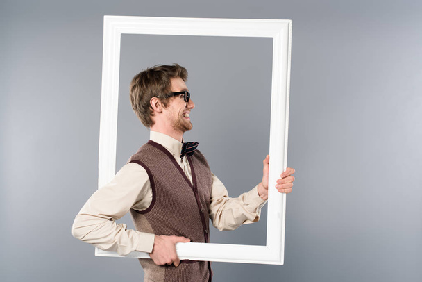 side view of smiling man holding white frame on grey background - 写真・画像