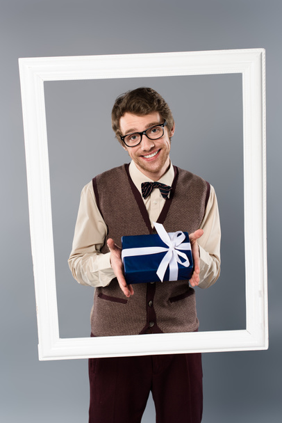 smiling man in white frame holding gift box on grey background - Фото, изображение