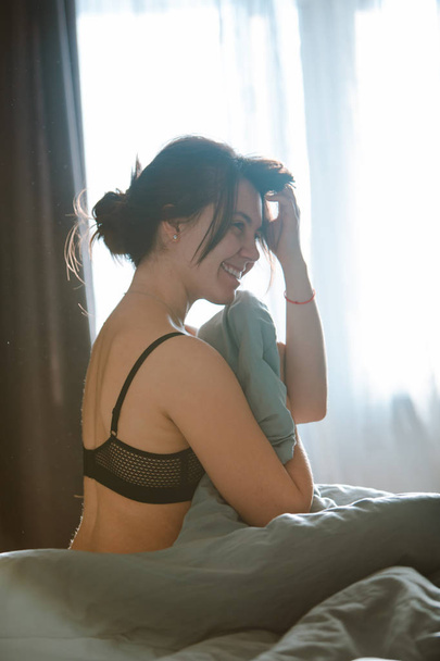 Młoda ładna kobieta w bra czarny, siedząc na łóżku. rano czasu - Zdjęcie, obraz