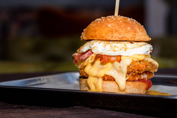 Close up tall tasty burger with cheese and egg served on tray - 写真・画像