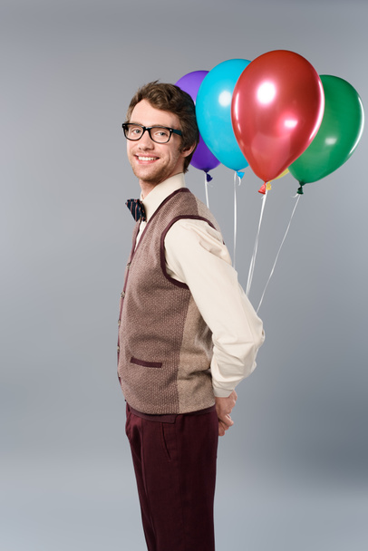 happy man in glasses holding multicolored balloons on grey background - Photo, Image