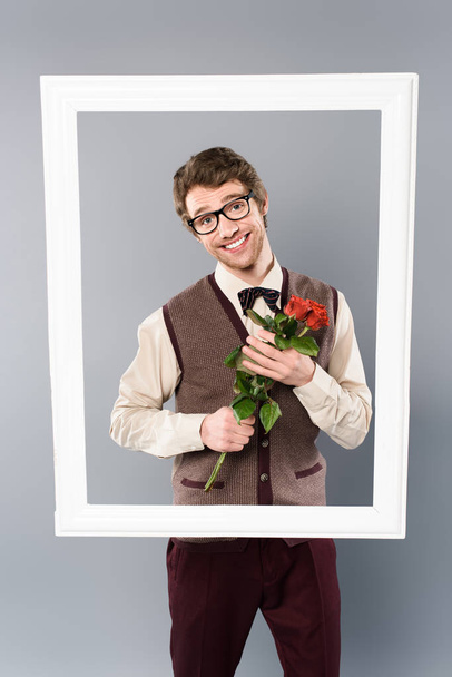 smiling man in white frame holding bouquet of roses on grey background - Photo, Image