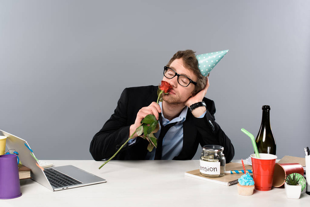drunk businessman in birthday cap smelling rose at workplace - Fotografie, Obrázek