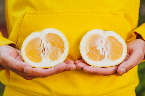 a man in a yellow hoodie is holding two halves of a yellow citrus cut in half. healthy eating, proper nutrition, organic food, close-up, conceptual photo. - Photo, Image