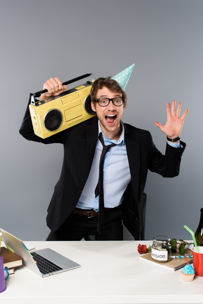 灰色の背景にヴィンテージのテープ レコーダーを持つパーティー キャップで職場で幸せなビジネスマン - 写真・画像