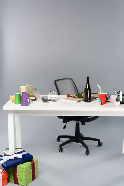 messy workplace with champagne bottle, paper cups, pension moneybox and laptop on white table near gift boxes - Foto, Bild