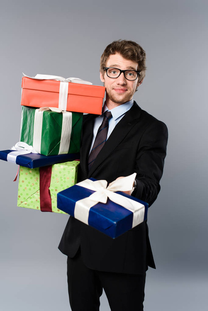 smiling businessman in glasses holding presents on grey background - Foto, immagini
