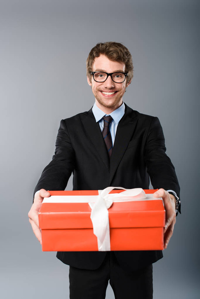 happy businessman holding orange present on grey background - Фото, зображення