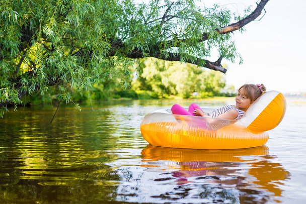 Little girl relaxes in an inflatable chair, floating on the water. - Foto, afbeelding