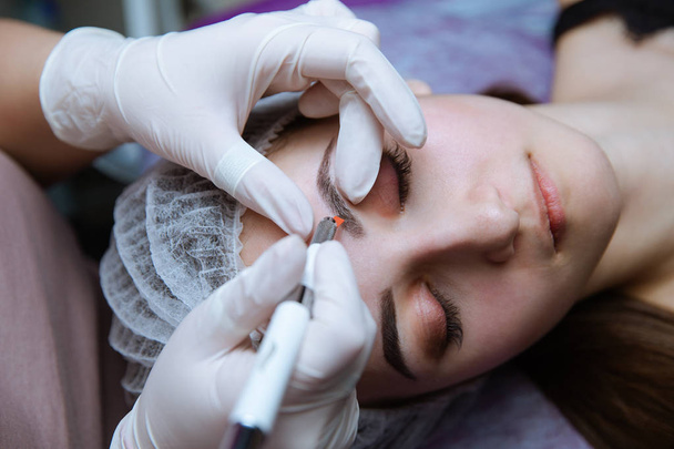 Maquiagem permanente para sobrancelhas. Testa de Microblading. Esteticista fazendo tatuagem de sobrancelha para rosto feminino. Menina bonita em uma beleza
 - Foto, Imagem