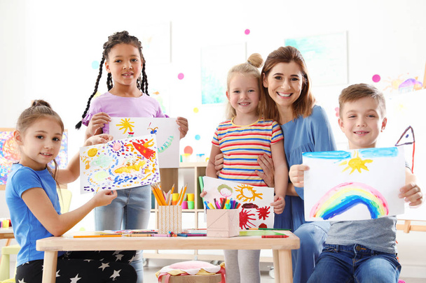 Carino i bambini piccoli con insegnante che mostra i loro dipinti a lezione in casa
 - Foto, immagini