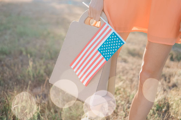 Memorial day sale, Independence day sale. Female hand with paper bag and american flag in spring or summer park - Fotoğraf, Görsel