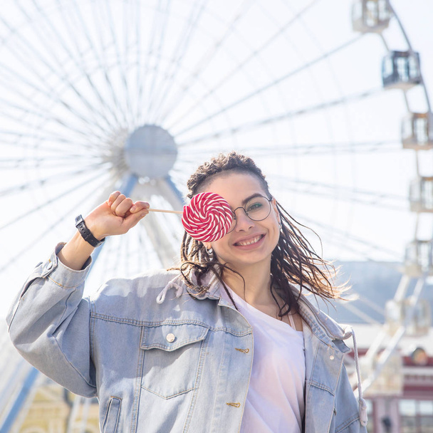 Beautiful caucasian girl with a lollipop in an amusement park - Fotoğraf, Görsel