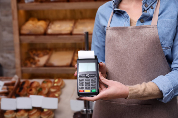 Woman holding payment terminal in bakery, closeup. Space for text - 写真・画像
