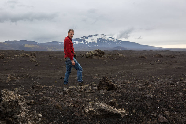 man stands on a stone on a scorched lava field - Zdjęcie, obraz