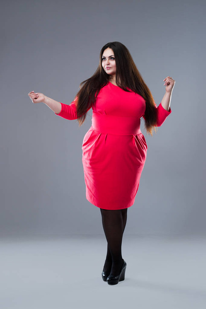 Brunette plus size fashion model in red dress, fat woman with long hair on gray background, body positive concept - Zdjęcie, obraz