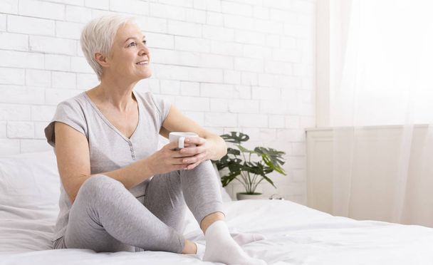Delighted senior woman relaxing in bed with cup of hot tea - Foto, immagini