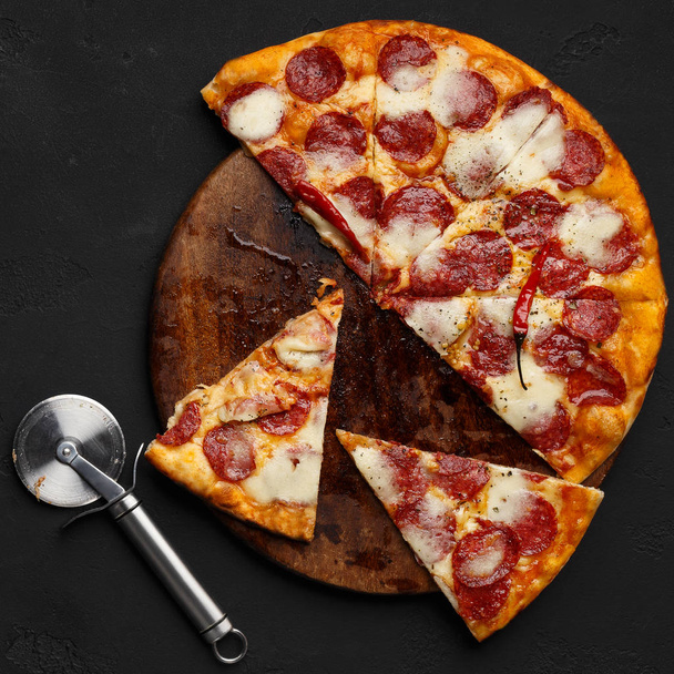 geschnittene Peperoni-Pizza auf Schneidebrett mit Cutter in der Nähe - Foto, Bild