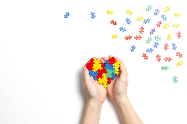 Criança mão segurando coração colorido no fundo branco. Conceito de Dia Mundial do Autismo
 - Foto, Imagem