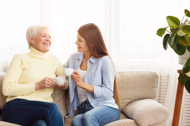 Young woman visiting senior mother and drinking coffee together - Foto, afbeelding