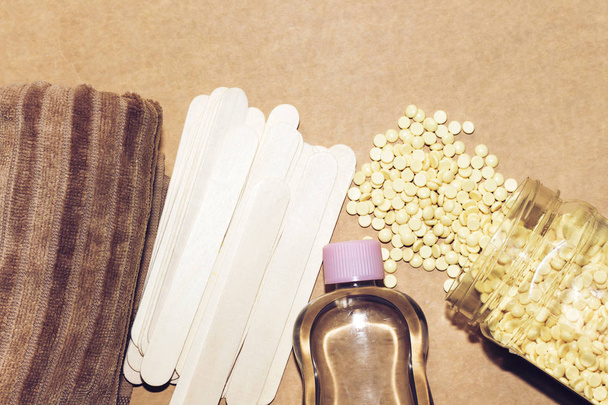 depilativní perlově žluté pevné voskové fazole a dřevěné tyčinky a olejová láhev - Fotografie, Obrázek