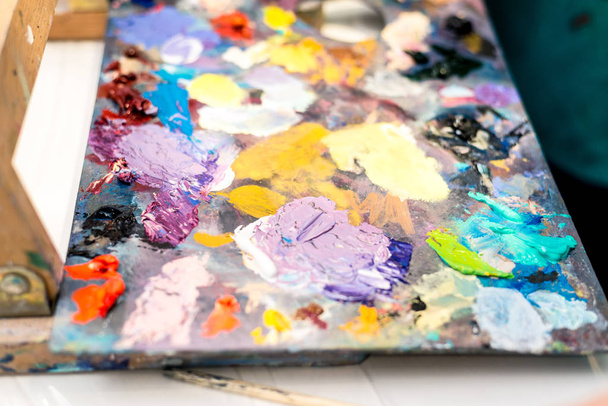 Paints of different colors on a multi-colored palette of mixed oil paints - Foto, afbeelding