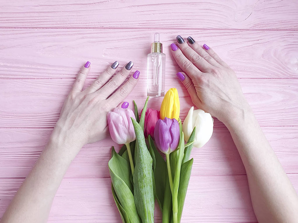 cosmetic extract, female hands, a bouquet of tulips on a pink wooden background - Фото, изображение