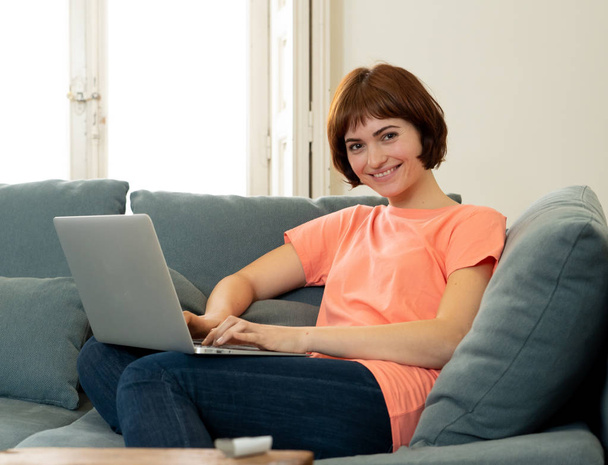 Lifestyle portrait of young attractive and relaxed woman using computer, enjoying watching online movie, working or studying at home smiling happy on the couch. In internet and social network concept. - Photo, image