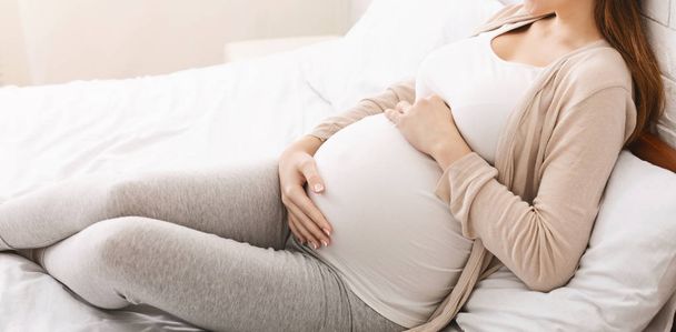 Счастливая беременная женщина ласкает живот, лежит в постели
 - Фото, изображение