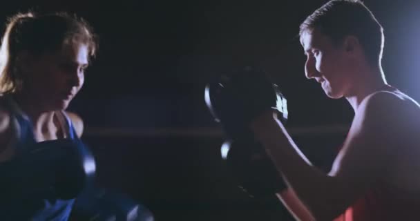 Female boxer punching a focus mitts with boxing gloves in a smoky gym - 映像、動画