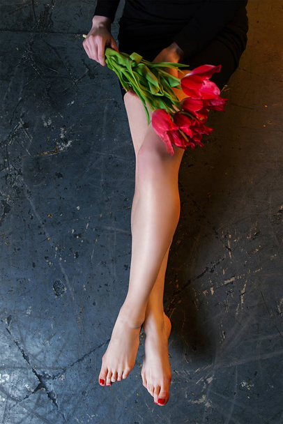 Motif des jambes de belle femme mince et lisse après épilation au laser sur le fond de ciment grossier avec des fleurs de tulipes
 - Photo, image