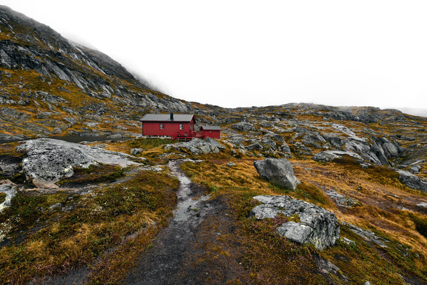 Trilha de caminhada que leva a uma cabine de madeira vermelha remota nas montanhas no Lofoten, na Noruega. A cabana está localizada na montanha Munken (Moskenesoy) e chamada Munkebu. A paisagem é composta por rochas, pedras e grama laranja e musgo
. - Foto, Imagem