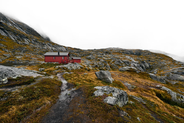 Wanderweg zu einer abgelegenen roten Holzhütte in den Bergen auf den Lofoten in Norwegen. Die Hütte befindet sich am Berg munken (moskenesoy) und wird munkebu genannt. Die Landschaft besteht aus Felsen, Steinen und orangefarbenem Gras und Moos. - Foto, Bild