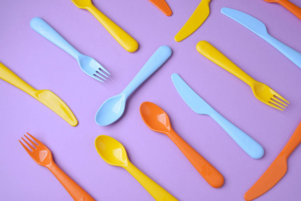 Many colorful plasic forks, spoons and knives on violet backgrou - 写真・画像