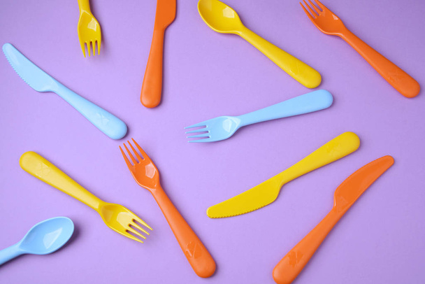 Many colorful plasic forks, spoons and knives on violet backgrou - Foto, Imagen