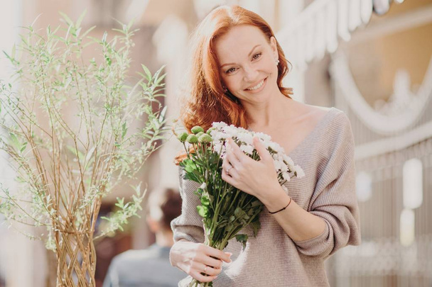 Venkovní snímek báječná žena foxy Naklonění hlavy, s přijímáním květiny od přítele, oblečený v neformálním oblečení, má datum wth přítele. Atraktivní červené vlasy žena ráda jaro. Pouliční styl - Fotografie, Obrázek