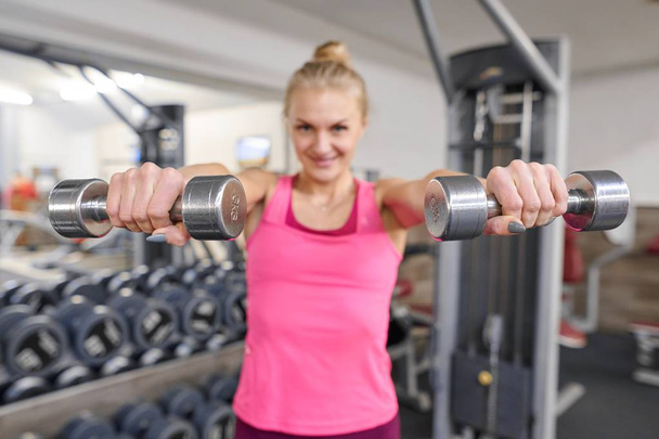 Young sporty blond woman in the gym. Woman holding metal weights, focus on kettlebells. People fitness sport healthy lifestyle concept - Zdjęcie, obraz