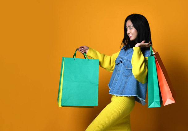 Young asian woman with shopping bags on color background - Φωτογραφία, εικόνα