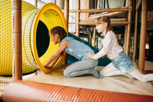 Δύο κοριτσάκια που σκαρφαλώνουν στο λαβύρινθο στο κέντρο παιχνιδιών για παιδιά. Ενθουσιασμένα παιδικά που διασκεδάζουν στην παιδική χαρά σε εσωτερικούς χώρους. Παιδιά που παίζουν στο κέντρο ψυχαγωγίας - Φωτογραφία, εικόνα