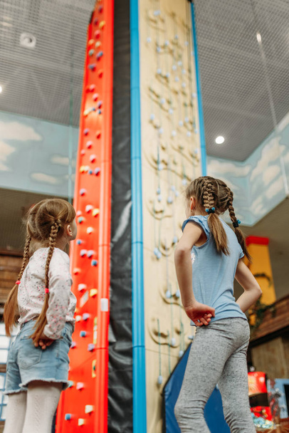 Deux petites filles regardent le mur d'escalade, centre de jeux pour enfants. Des enfants excités s'amusent sur une aire de jeux à l'intérieur. Enfants jouant dans un centre de divertissement
 - Photo, image