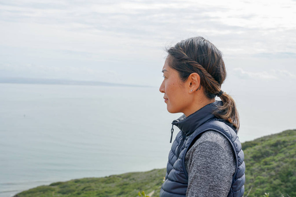 Young sporty Asian woman looking out at the beautiful ocean view. Young woman hiker standing admiring the view. healthy active lifestyle. - Valokuva, kuva