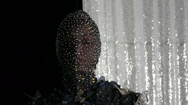 Haute couture. Modèle à l'image d'une fille étrangère dans un masque noir en strass étincelants, étincelles, papillons métalliques sur un fond noir et argenté posant dans un studio de mannequins
. - Séquence, vidéo