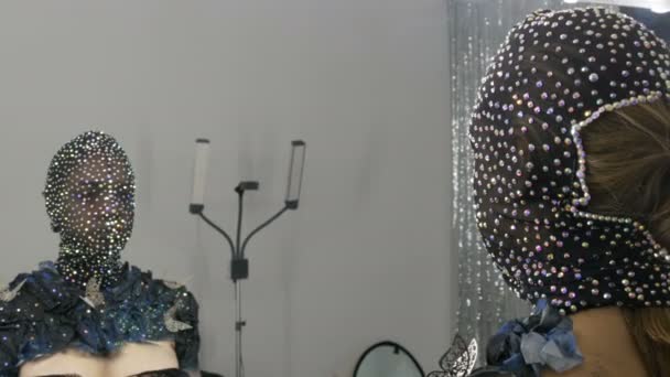 Hochmodisch. Modell im Bild eines fremden Mädchens mit schwarzer Maske in glitzernden Strasssteinen, Funkeln, Metallschmetterlingen auf schwarz-silbernem Hintergrund, die im Studio vor dem Spiegel posieren - Filmmaterial, Video