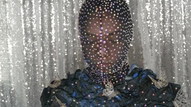 De alta moda. Modelo na imagem de uma menina alienígena em uma máscara preta em strass espumantes, brilhos, borboletas de metal em um fundo preto e prata posando em um estúdio modelo
. - Filmagem, Vídeo