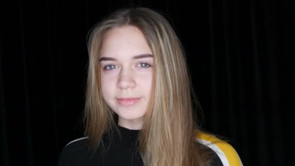 Portret van een mooie jonge tiener meisje met lange witte haren en groene ogen poseren gek rond glimlachen en het aanraken van haar haar in de voorkant van de camera in de studio op een zwarte achtergrond - Video