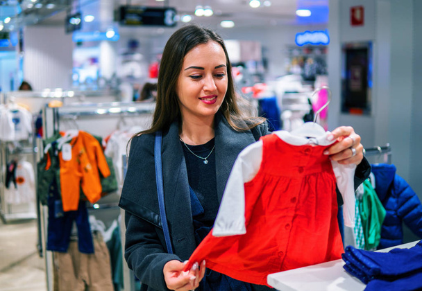 Cliente mulher escolhendo roupas de bebê na loja
 - Foto, Imagem